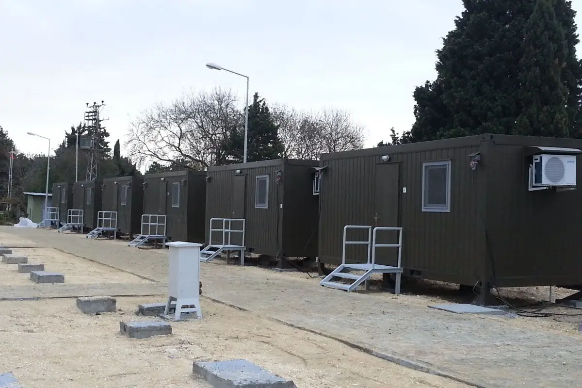 Sıra halinde dizilmiş, klimalı ve merdivenli, askeri yeşil prefabrik konteyner yaşam üniteleri; askeri kamp ve şantiye yerleşkesi çözümü.