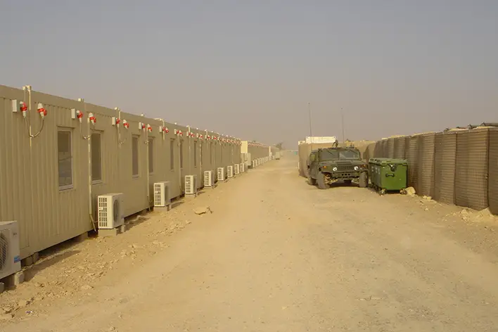 Zorlu arazi koşullarında kullanılan, yan yana dizilmiş klimalı prefabrik askeri konteynerler ve operasyonel bir kamp alanı görüntüsü.